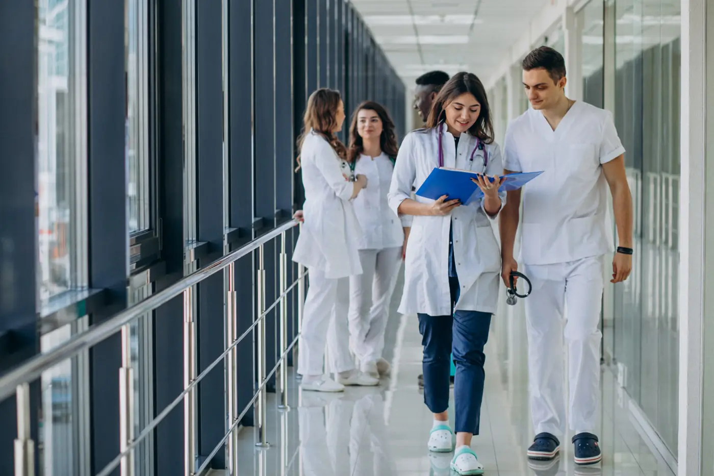 Two medical students walking a hospital corridor, reading the same folder of notes together.